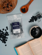 Packaged blueberries with a bowl of blueberries and an open book on a light blue background